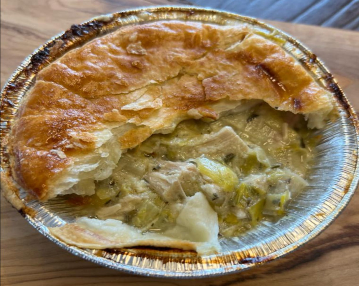 Chicken pieces with Sautéed leeks in a herb white wine sauce, topped with a flaky puff pastry lid, cut in half.